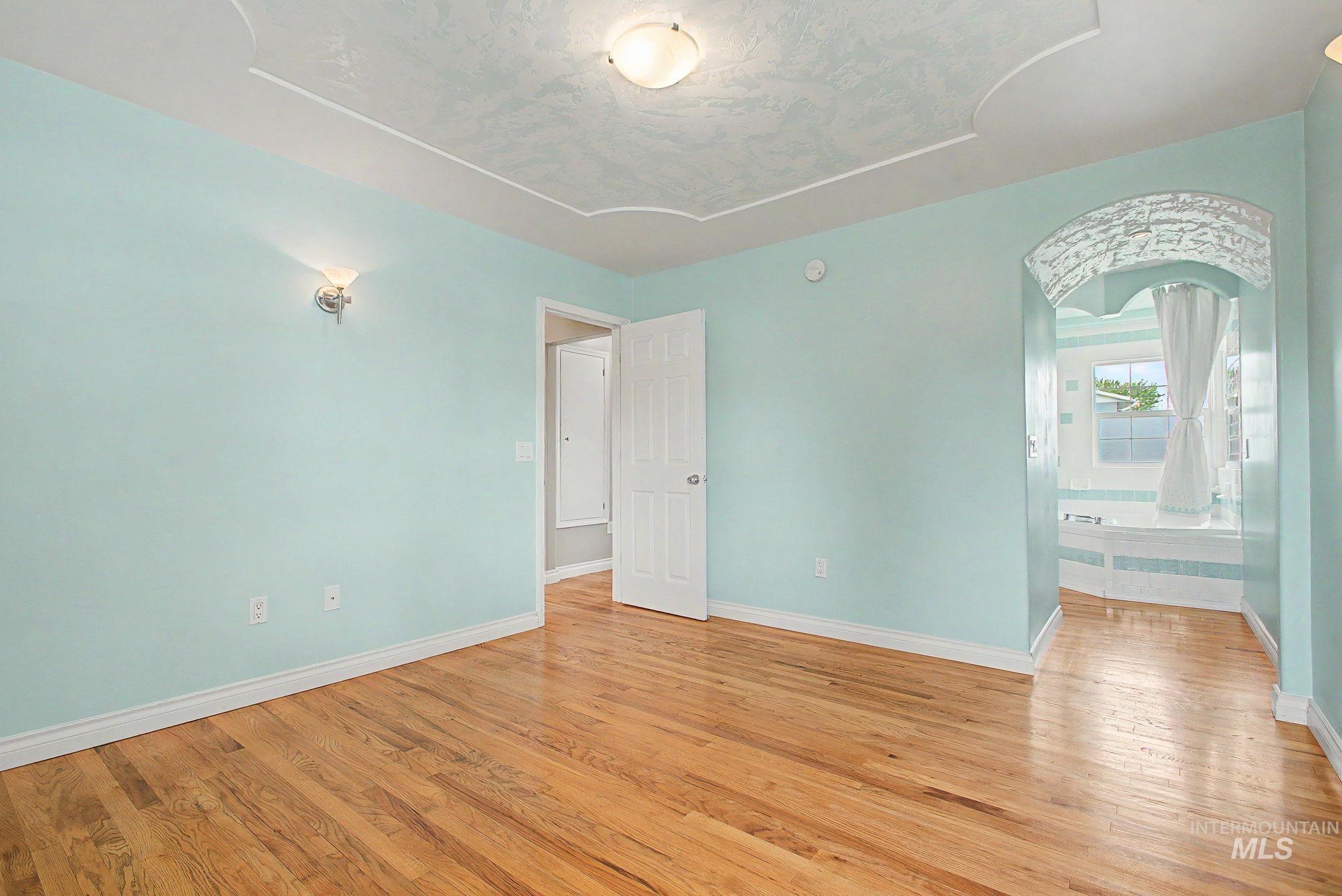 3314 6th Street Lewiston, ID 83501 - Photo 21 of 50 Bedroom featuring hardwood flooring, an arched entry to a bathroom, a decorative tray ceiling, and a wall sconce