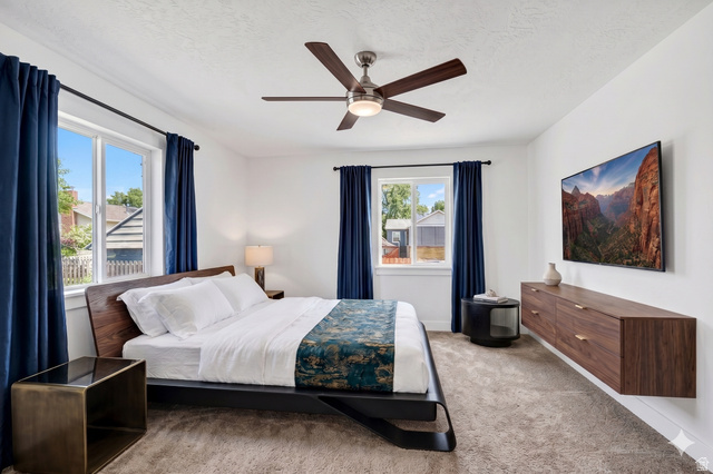 7879 Oak Street Midvale, UT 84047 - Photo 10 of 32 Bright room featuring two windows with dark blue drapes, a ceiling fan, and carpeted flooring