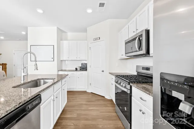 a kitchen with stainless steel appliances granite countertop white cabinets a stove a sink and a refrigerator