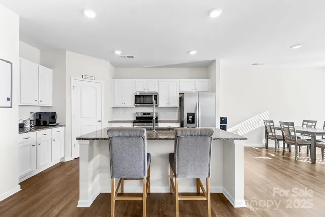 a kitchen with stainless steel appliances granite countertop a stove top oven a sink a refrigerator with white cabinets and wooden floor