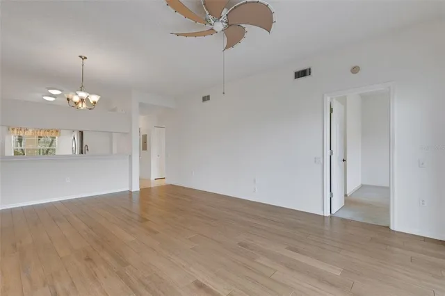 an empty room with wooden floor chandelier fan and windows
