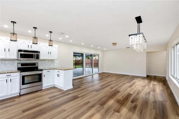 a open kitchen with stainless steel appliances granite countertop a sink dishwasher a refrigerator and a fireplace with wooden floor