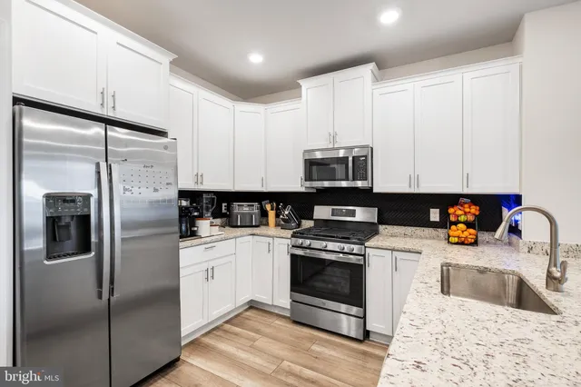 a kitchen with stainless steel appliances granite countertop a refrigerator sink and white cabinets