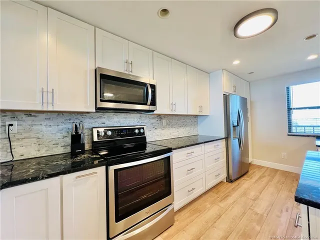 a large kitchen with stainless steel appliances granite countertop a refrigerator a oven and white cabinets with wooden floors