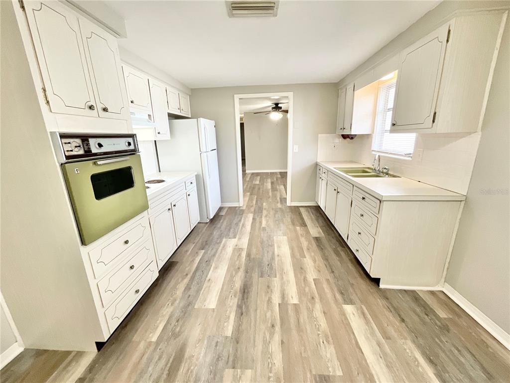 1541 Alert Street Holiday, FL 34690 - Photo 7 of 17 a large white kitchen with sink a stove a refrigerator with white cabinets and wooden floor