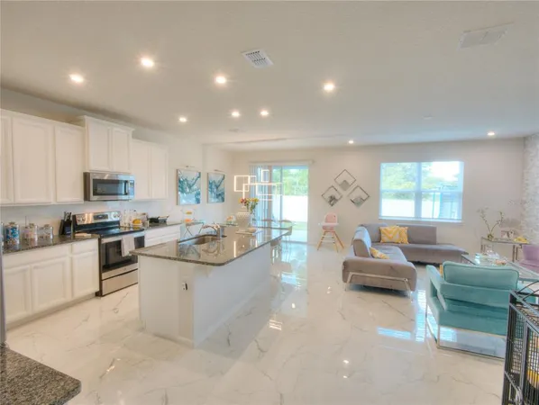 a living room with stainless steel appliances kitchen island granite countertop a refrigerator a stove top oven a sink dishwasher and white cabinets with wooden floor