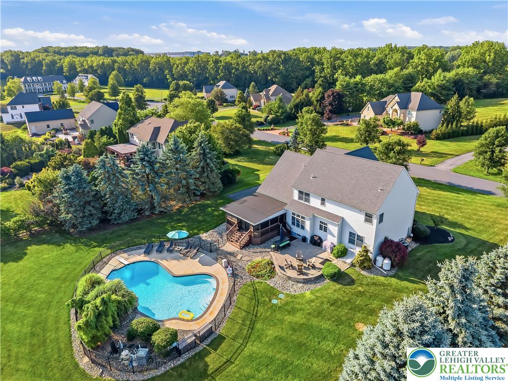 13 Country Road Northampton, PA 18067 - Photo 7 of 71 A heart-shaped pool and spacious patio create an idyllic backyard oasis, surrounded by lush greenery and neighborhood homes.