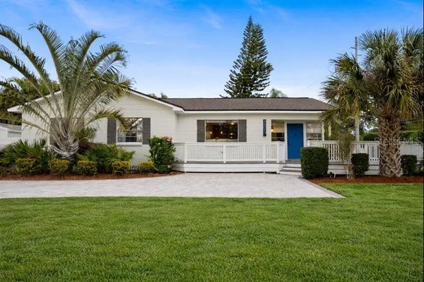 a view of a white house next to a yard with palm trees