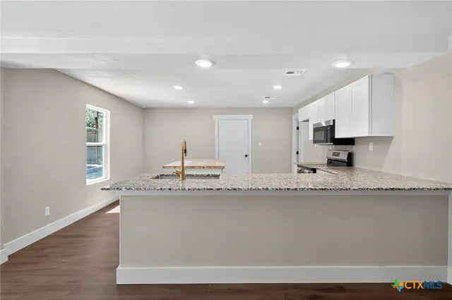 a large white kitchen with granite countertop a sink window and a granite counter top