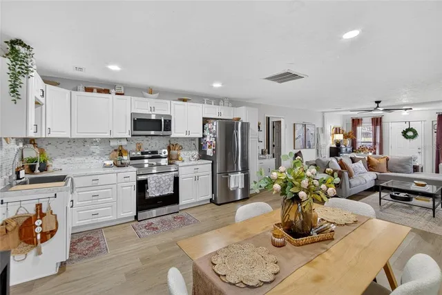 a kitchen with stainless steel appliances granite countertop a refrigerator a stove a sink a dining table and chairs with wooden floor