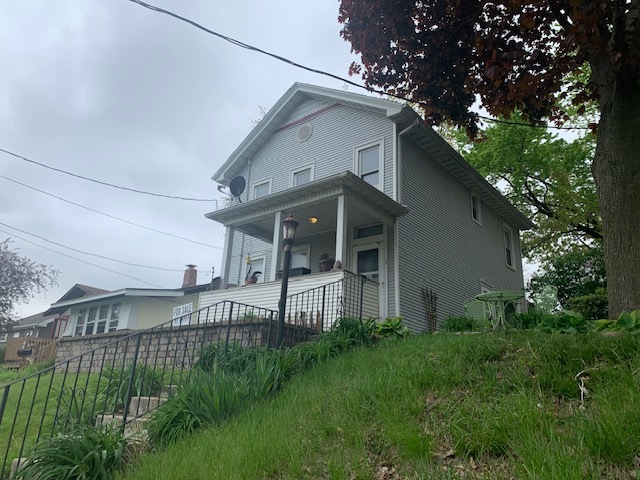 a view of a white house next to a yard with plants and large trees