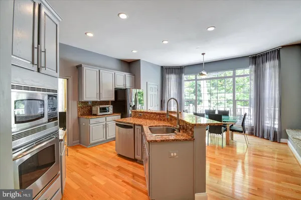 a kitchen with stainless steel appliances granite countertop a stove top oven a sink dishwasher a dining table and chairs with wooden floor