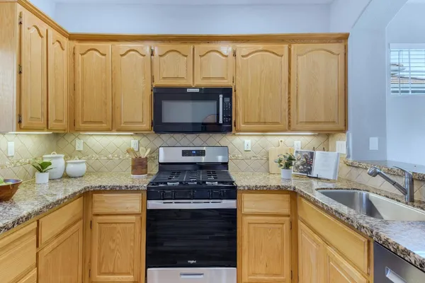 a kitchen with granite countertop a sink a stove top oven a counter space and cabinets