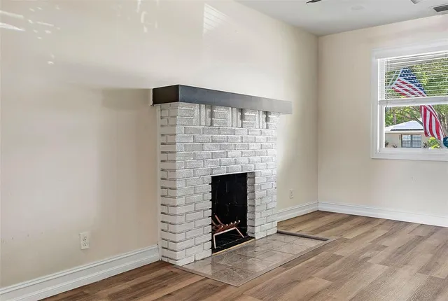 an empty room with wooden floor fireplace and windows
