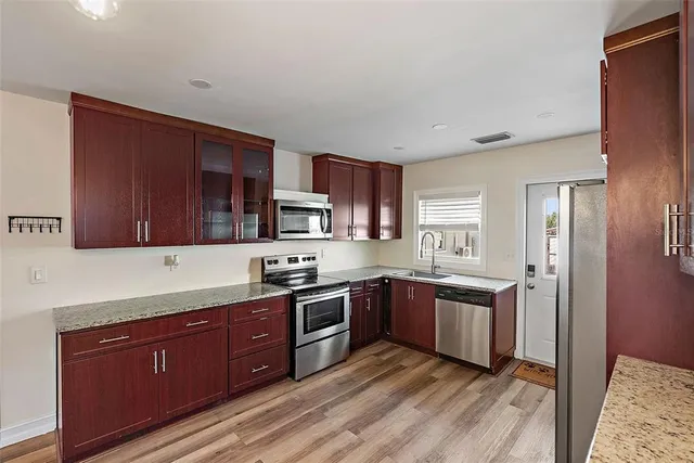 a kitchen with stainless steel appliances granite countertop wooden cabinets a sink dishwasher a stove and a refrigerator with wooden floor