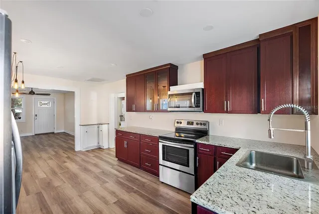 a kitchen with stainless steel appliances granite countertop a stove top oven a sink dishwasher and a refrigerator with wooden cabinets