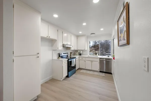a kitchen with a white refrigerator stove a sink and white cabinets with wooden floor