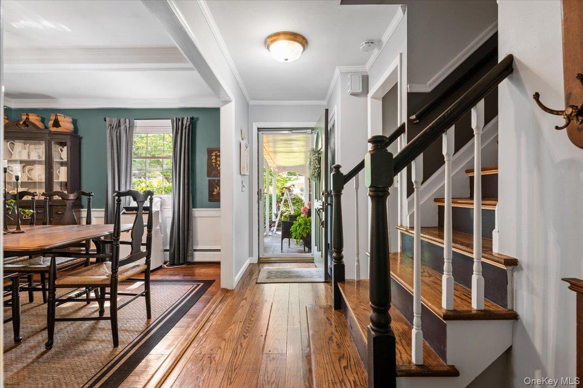 10 Rancher Place Huntington, NY 11743 - Photo 3 of 44 Hardwood flooring throughout entryway and dining area, featuring a staircase with contrasting dark wood handrails and white balusters, and a dining space with decorative wainscoting and a window