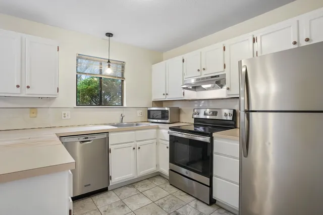 a kitchen with white cabinets appliances and a window