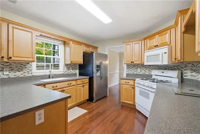a kitchen with stainless steel appliances granite countertop a refrigerator a stove and a sink with wooden floors