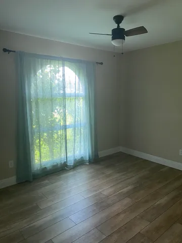 an empty room with wooden floor fan and windows