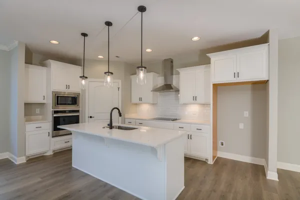 a large kitchen with stainless steel appliances kitchen island a refrigerator a stove a oven and white cabinets with wooden floor