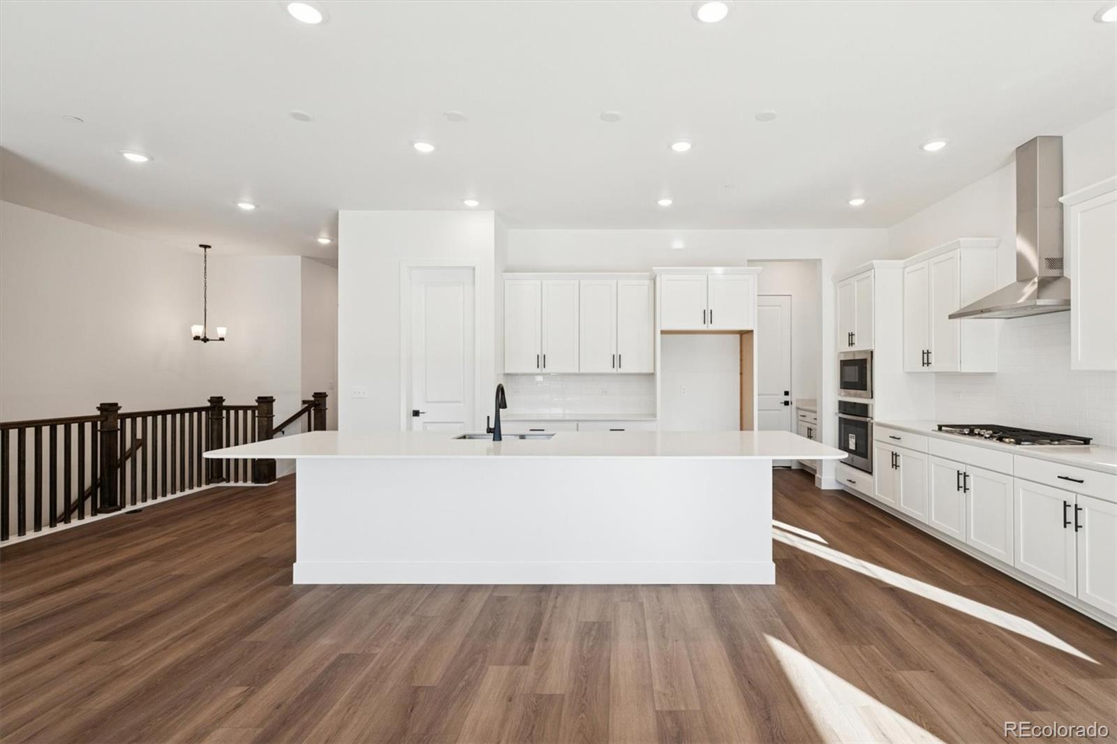 1242 Summit Rise Drive Erie, CO 80516 - Photo 12 of 25 a large white kitchen with wooden floors stainless steel appliances and white cabinets
