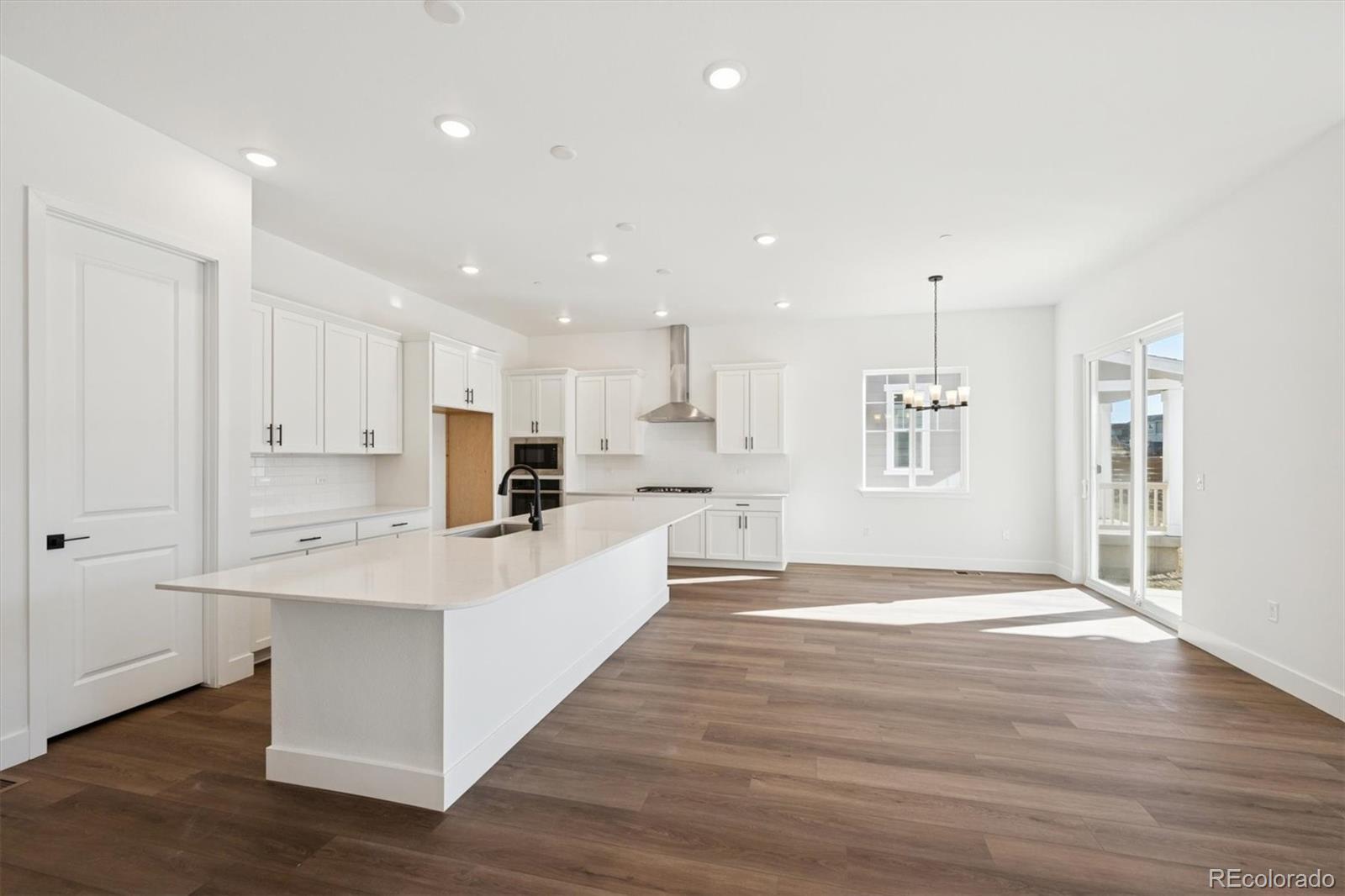 1242 Summit Rise Drive Erie, CO 80516 - Photo 9 of 25 a large white kitchen with kitchen island a sink wooden floor and white cabinets