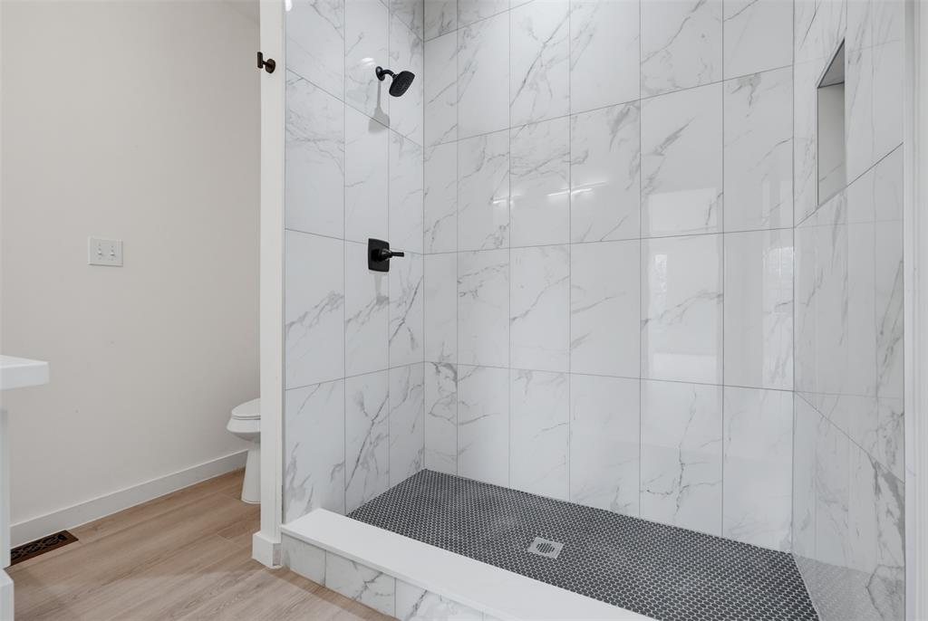 516 South O Connor Road Irving, TX 75060 - Photo 16 of 23 Walk-in shower featuring white marble-look subway tile, a dark penny tile floor, a built-in shower niche, and matte black fixtures