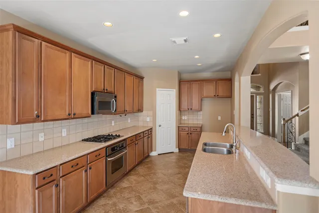 a large kitchen with stainless steel appliances granite countertop a large counter top a stove a chimney a sink and a refrigerator