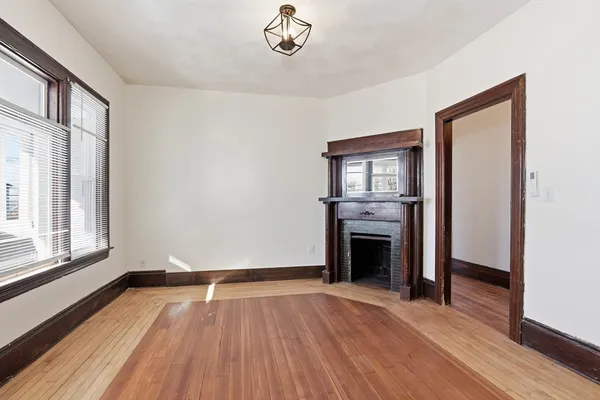 a view of an empty room with wooden floor fireplace and a window
