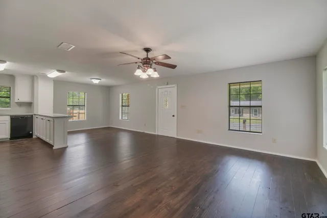 a view of an empty room with wooden floor and a kitchen