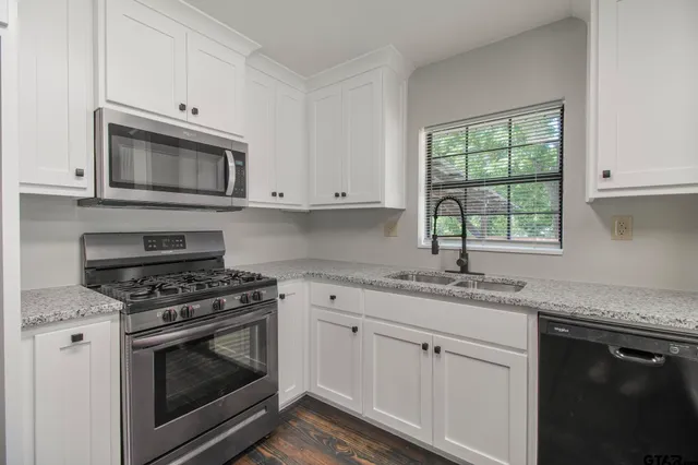 a kitchen with granite countertop white cabinets appliances and a window