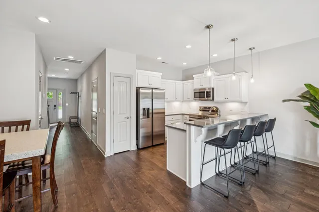 a kitchen with stainless steel appliances kitchen island granite countertop a refrigerator a stove a sink a dining table and chairs with wooden floor