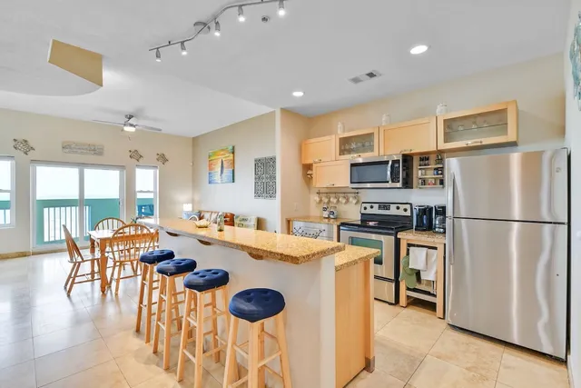 a kitchen with stainless steel appliances granite countertop a refrigerator a stove top oven a sink dishwasher a dining table and chairs with wooden floor