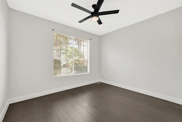 an empty room with wooden floor fan and windows