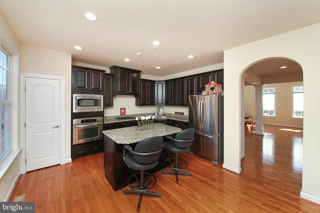 a kitchen with stainless steel appliances granite countertop a refrigerator a sink dishwasher a stove and a dining table with wooden floor