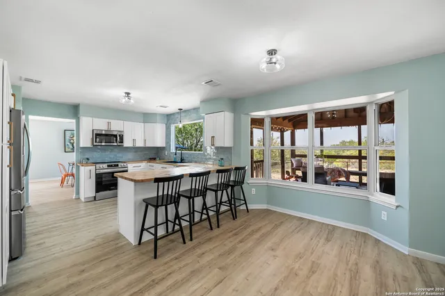 a kitchen with stainless steel appliances granite countertop a stove top oven a sink a dining table and chairs with wooden floor