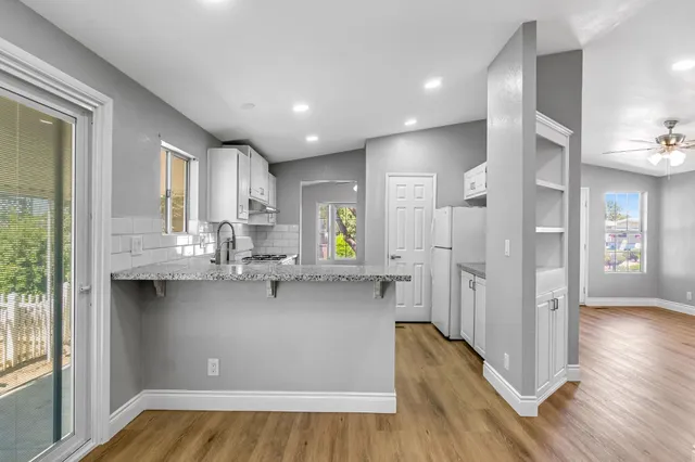 a kitchen with stainless steel appliances granite countertop a refrigerator a sink dishwasher a stove and white countertops with wooden floor