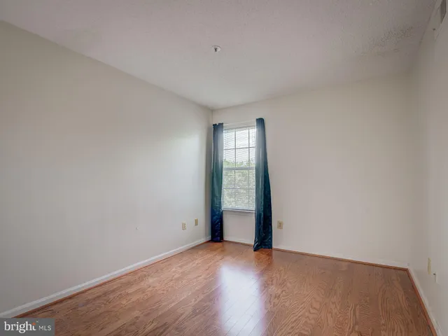 a view of an empty room with wooden floor and fan