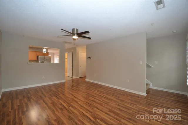 a view of an empty room with wooden floor and a ceiling fan