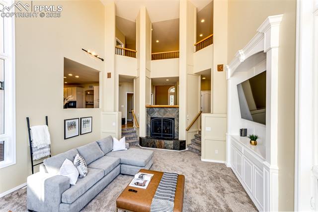 19340 Furrow Road Monument, CO 80132 - Photo 6 of 50 Living area featuring baseboards, a towering ceiling, stairway, a tiled fireplace, and light colored carpet
