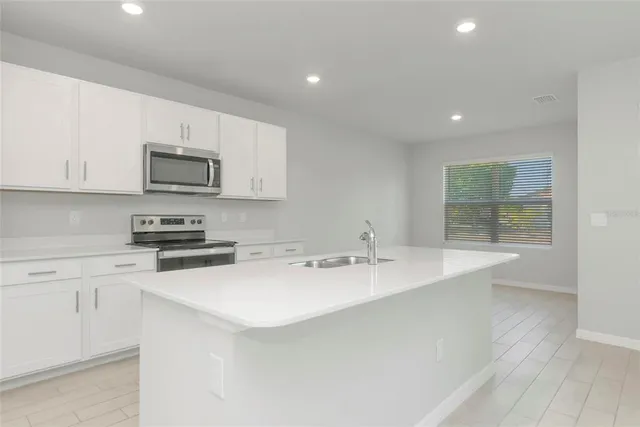 a kitchen with stainless steel appliances granite countertop a sink a stove a microwave a refrigerator a white cabinets and wooden floor