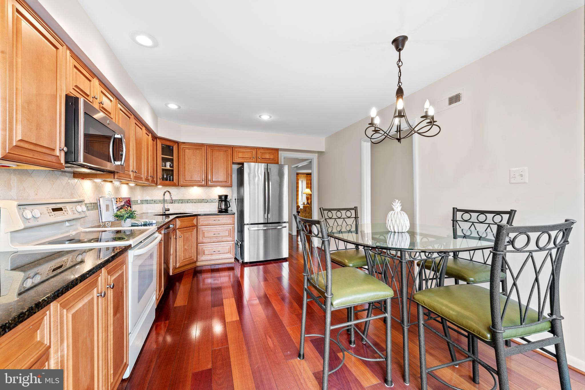 11711 Newbridge Court Reston, VA 20191 - Photo 11 of 37 a kitchen with stainless steel appliances kitchen island granite countertop a table chairs in it and wooden floors