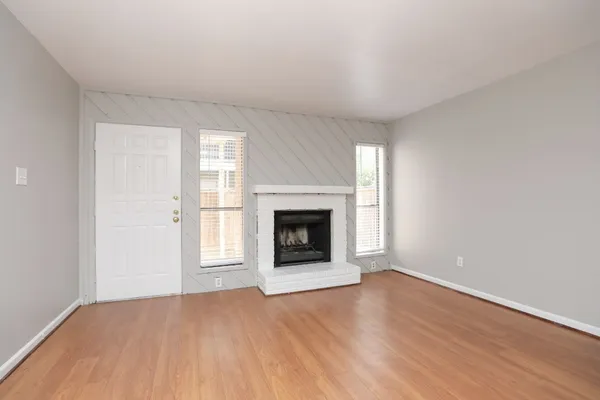 an empty room with wooden floor fireplace and windows