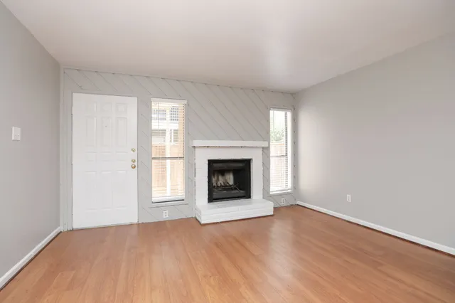 an empty room with wooden floor fireplace and windows