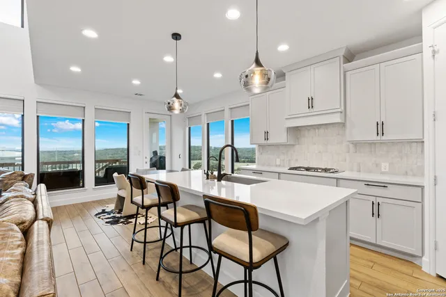 a kitchen with stainless steel appliances granite countertop a stove top oven a refrigerator a sink and white cabinets with wooden floor