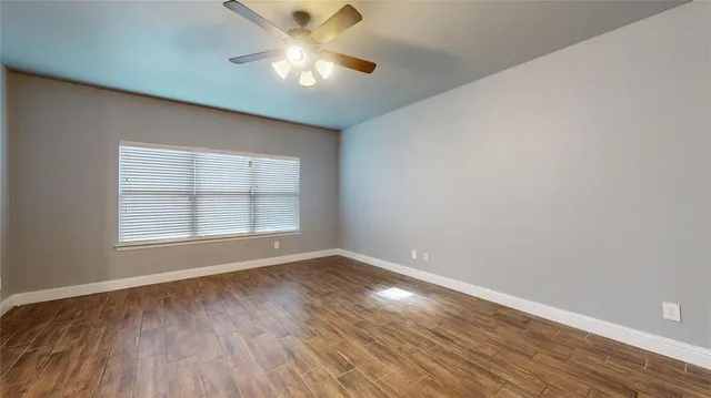 an empty room with wooden floor chandelier fan and windows