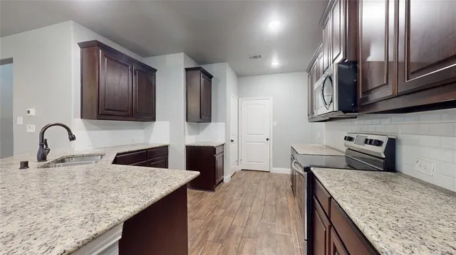 a kitchen with stainless steel appliances granite countertop a sink a stove and a wooden floors