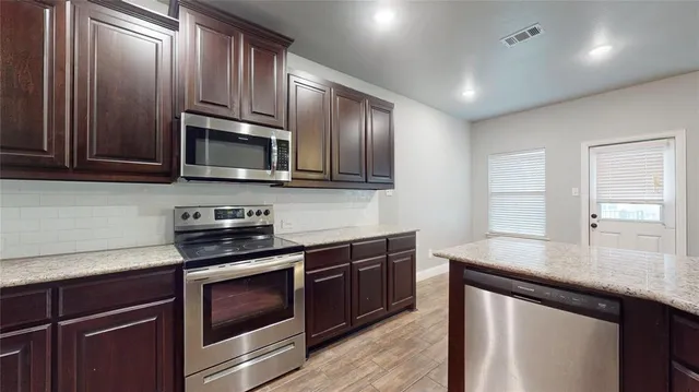 a kitchen with granite countertop wooden cabinets stainless steel appliances and a window